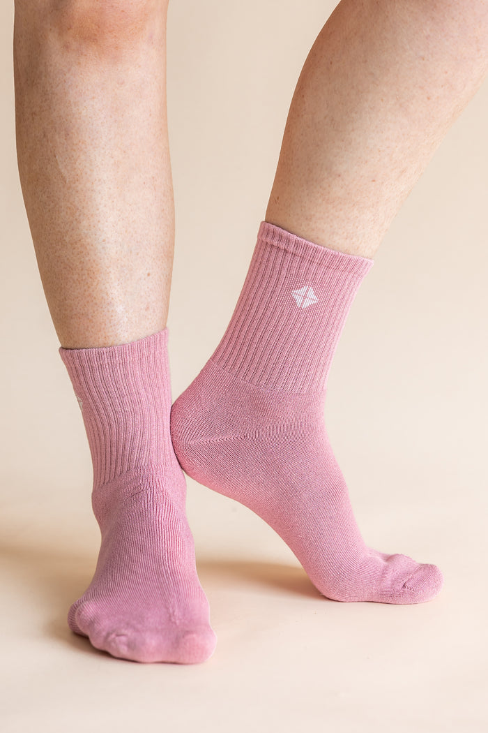 A pair of light pink ribbed ankle socks worn on a person's feet, shown against a solid light beige background.