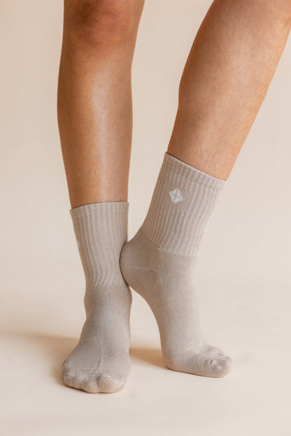 A close-up of a person's feet and lower legs wearing light gray ribbed crew socks against a warm beige studio background.