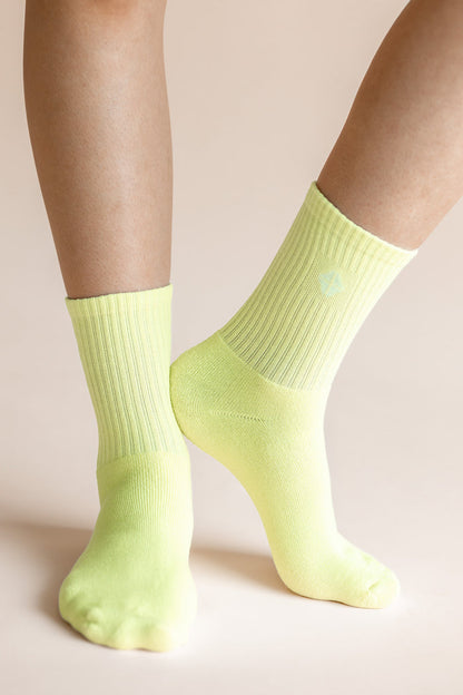 A close-up of a person's feet and lower legs wearing bright neon yellow-green crew socks against a solid pale beige background.