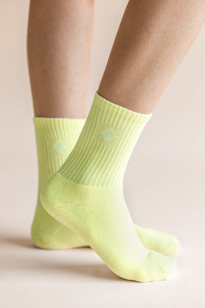 A close-up of a person's feet wearing light neon yellow crew socks against a soft beige background.