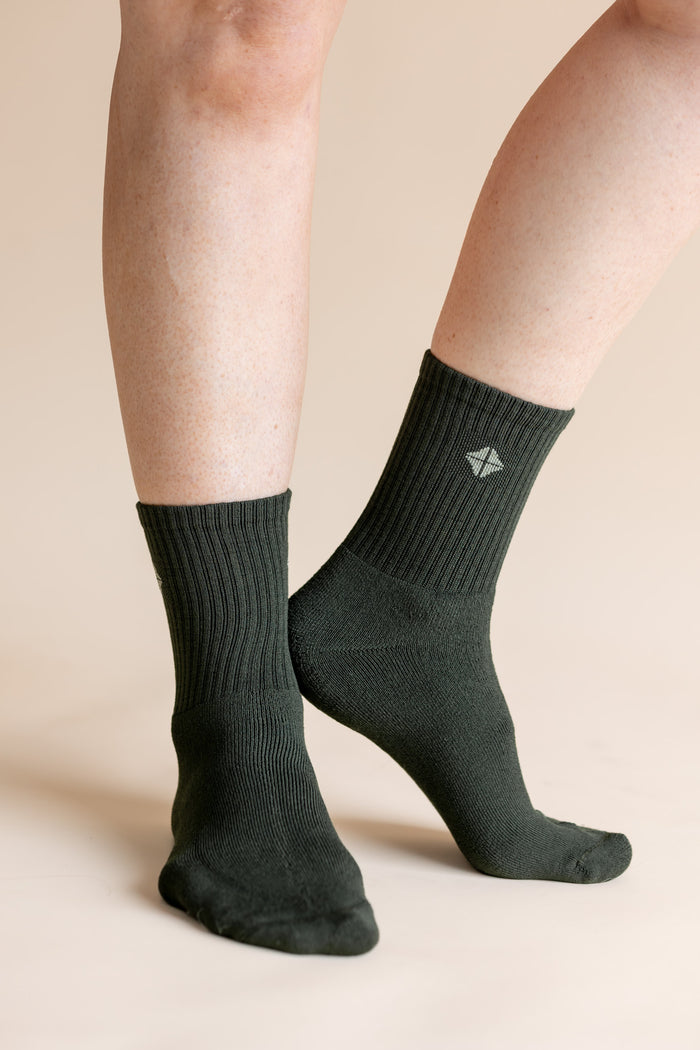 A close-up of a person's legs wearing dark forest green ribbed crew socks against a solid beige background.