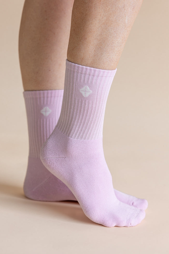 A pair of light lavender ribbed crew socks worn on feet, shown against a solid beige background.