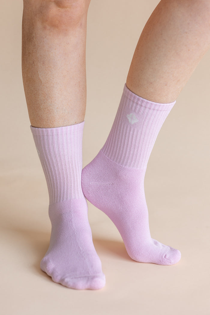 A close-up of a person's feet and lower legs wearing light lavender ribbed crew socks against a solid beige background.