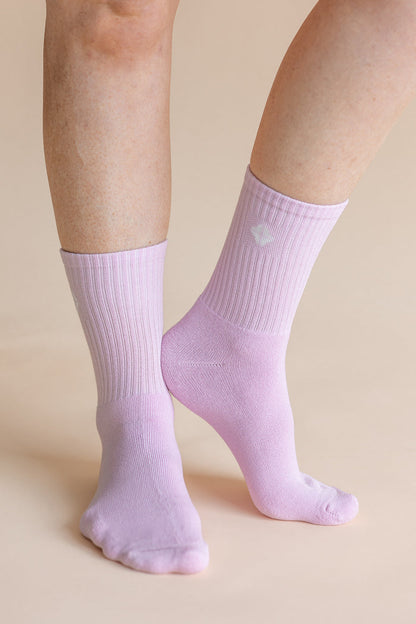 A close-up of a person's feet and lower legs wearing light lavender ribbed crew socks against a solid beige background.