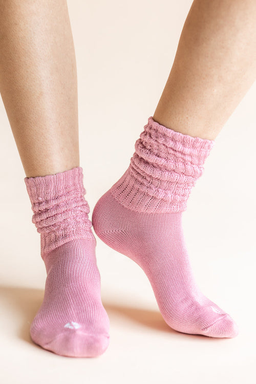 A pair of light pink ribbed scrunch socks worn on a person's feet, shown against a solid pale beige background.