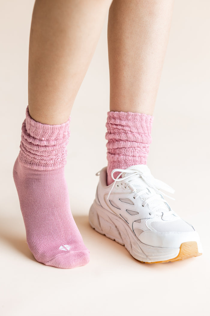 A close-up of a person's feet wearing a pair of light pink ribbed crew socks and white sneakers against a solid light beige background.