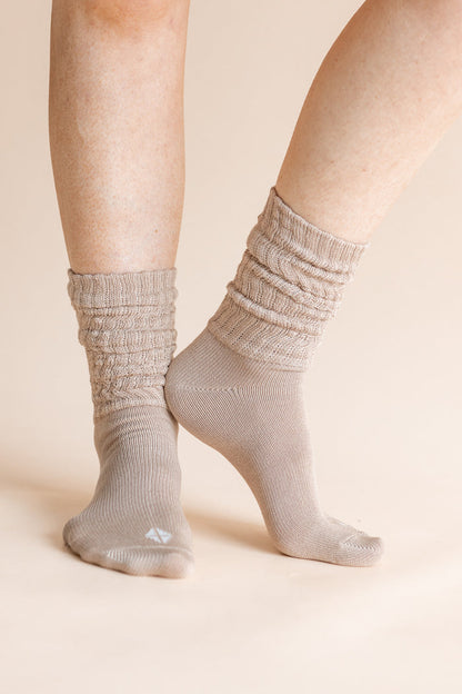 A close-up of a person's feet wearing light taupe ribbed crew socks against a solid beige background.
