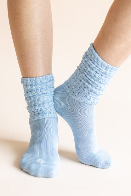 Light blue ribbed crew socks worn on a person's feet, shown against a plain warm beige background.