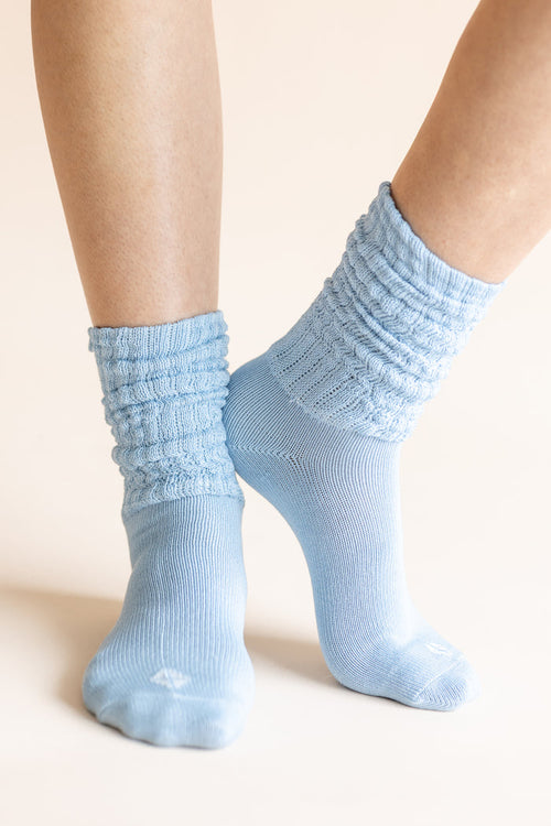 Light blue ribbed crew socks worn on a person's feet, shown against a plain warm beige background.