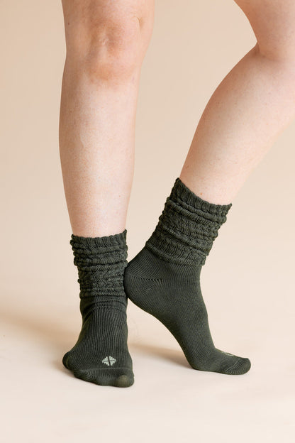 A close-up of a person's legs wearing dark olive green ribbed crew socks against a solid beige background.