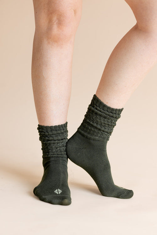 A close-up of a person's legs wearing dark olive green ribbed crew socks against a solid beige background.