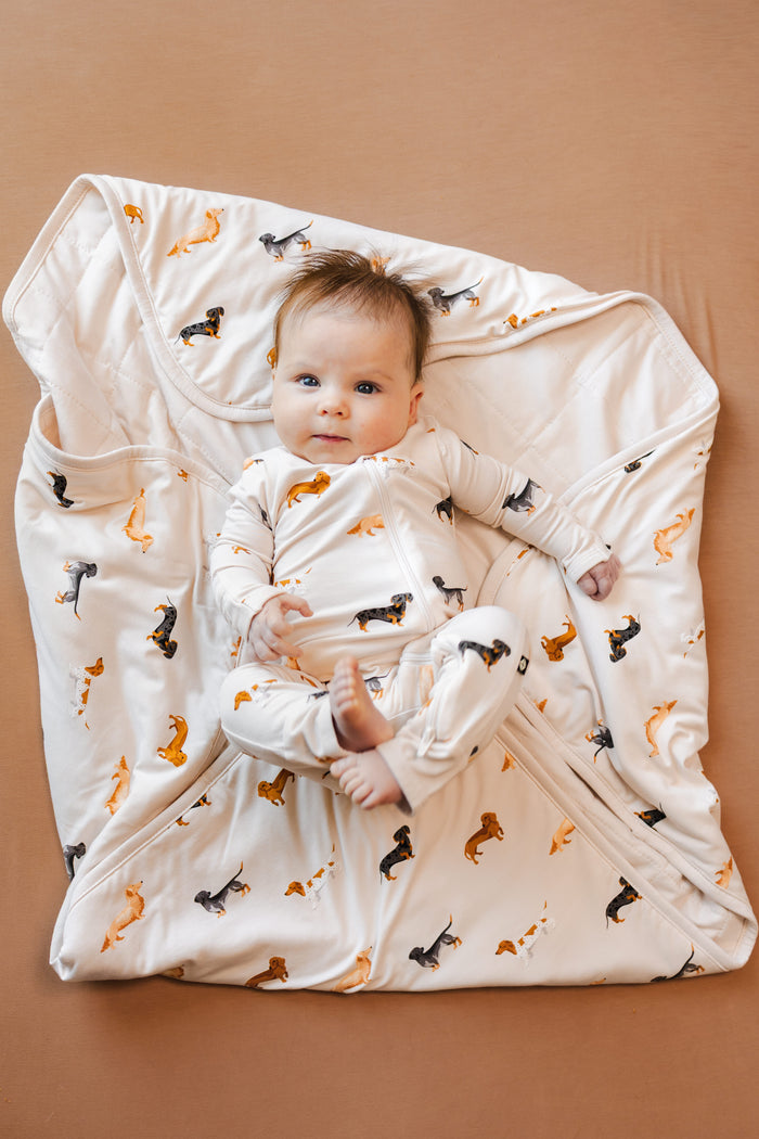 Baby lying over a beige Blanket with Dachshund print wearing a similar print romper on a brown background