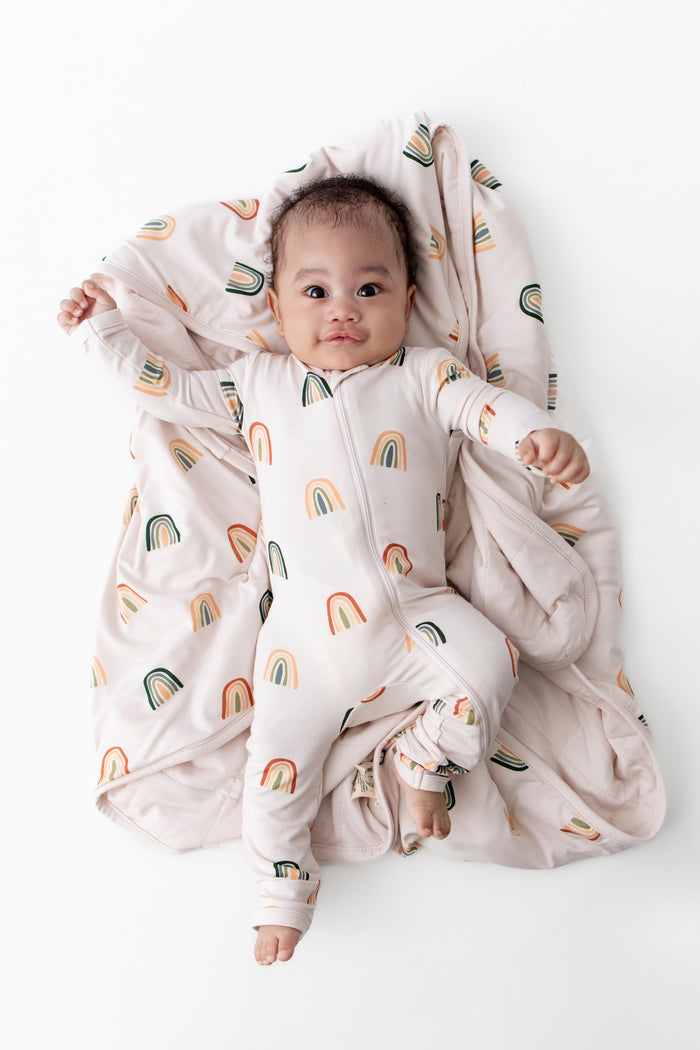 Baby lying on Baby Blanket with Retro Rainbow print wearing similar print zippered romper on a white background