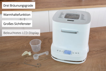 Der Unold AG Backmeister Bernd Weißbrotbackautomat steht auf einer hölzernen Arbeitsplatte mit Tasten und einem beleuchteten LCD-Display. Er enthält einen Messbecher, einen Löffel, einen Haken und ein Paddel und verfügt über drei Bräunungsstufen, Warmhaltefunktion und ein großes Sichtfenster.