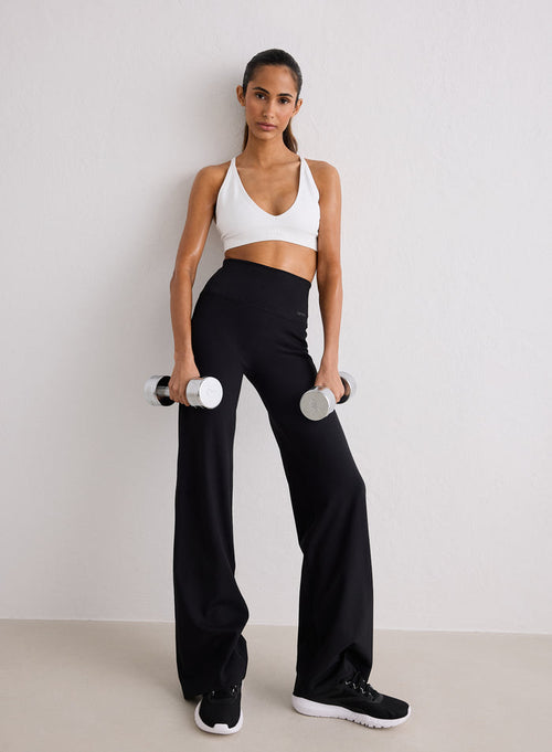 Woman in a white sports bra and Black Sense Straight Leg Petite Tights by aim'n holding dumbbells
