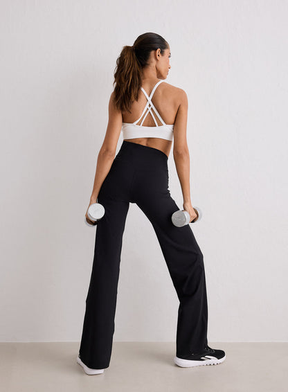 Rear view of a model wearing Black Sense Straight Leg Petite Tights and a white sports bra while holding dumbbells
