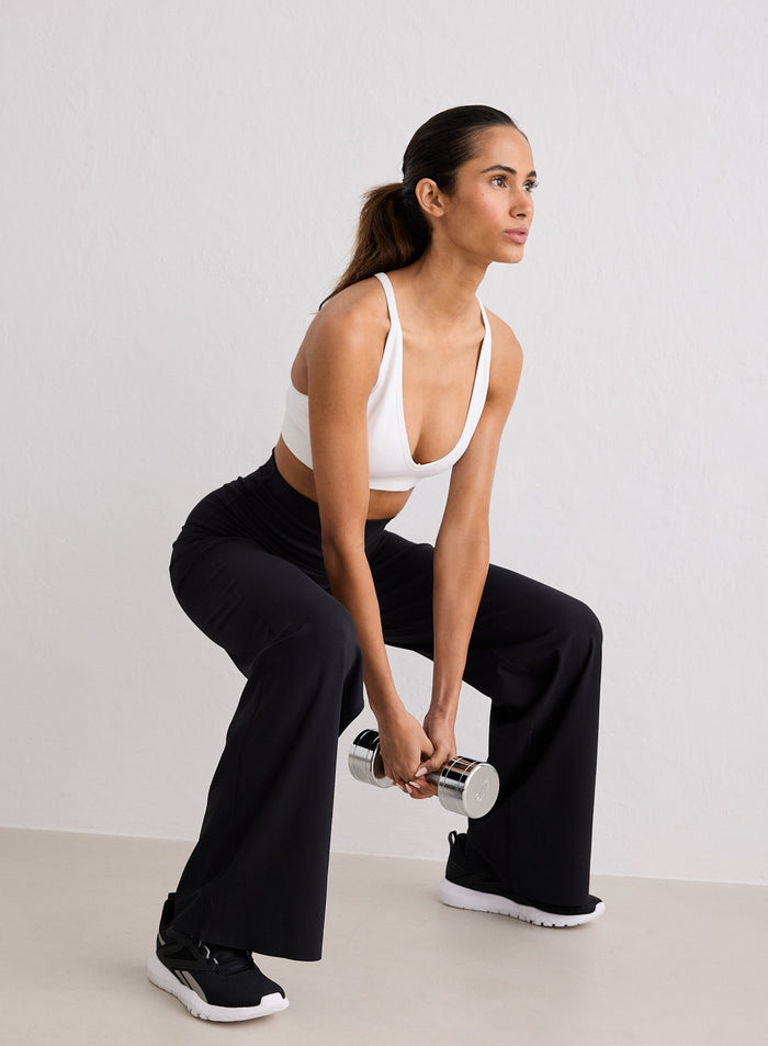 A woman performing a squat while holding a silver dumbbell, wearing Black Sense Straight Leg Petite Tights and a white sports bra