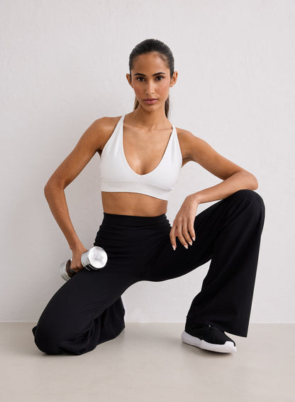A woman wearing a white sports bra and black Sense Straight Leg Petite Tights by aim'n, kneeling and holding a silver dumbbell