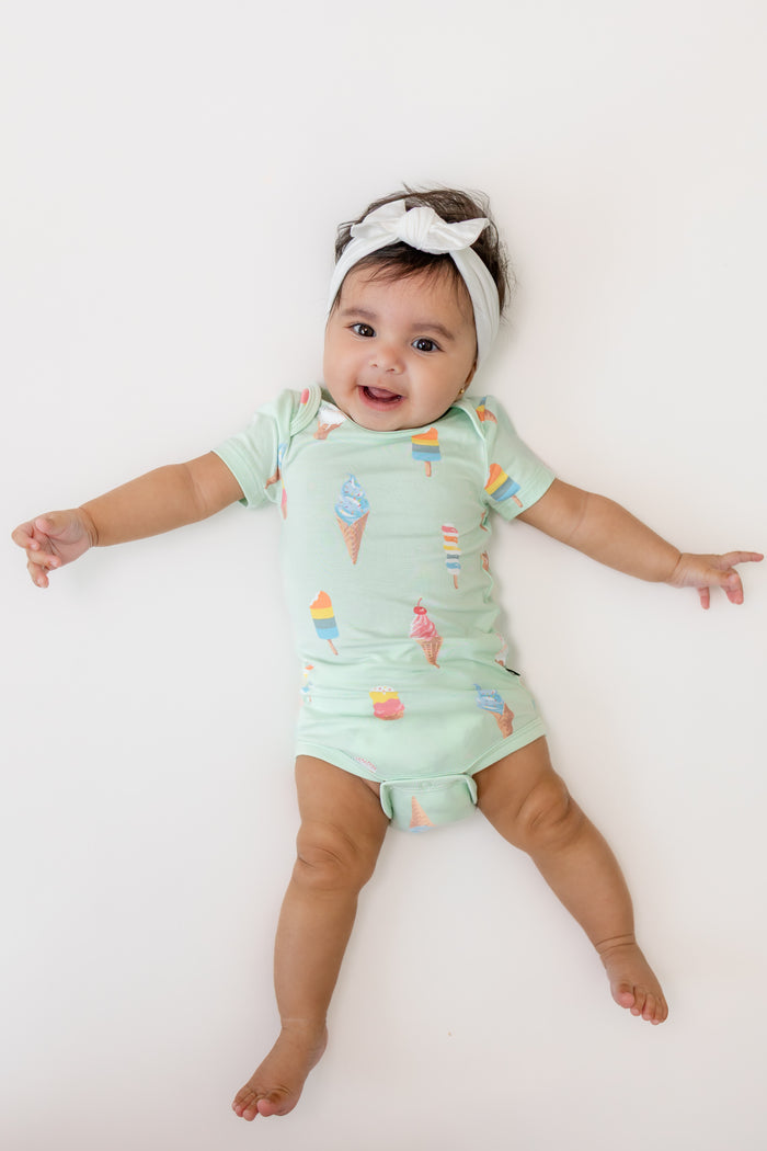 Baby wearing a Mint Ice cream print Bodysuit with a white Bow headband on a beige background
