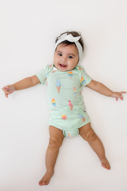 Baby wearing a Mint Ice cream print Bodysuit with a white Bow headband on a beige background