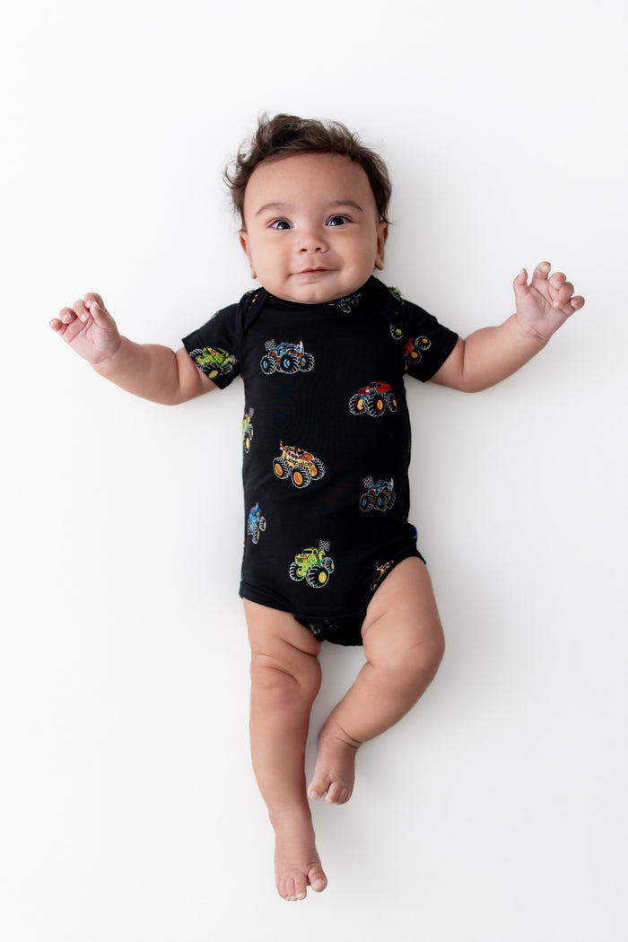 Baby lying in Black Bodysuit in Monster Truck print on white background