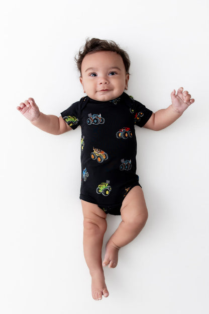 Baby lying in Black Bodysuit in Monster Truck print on white background
