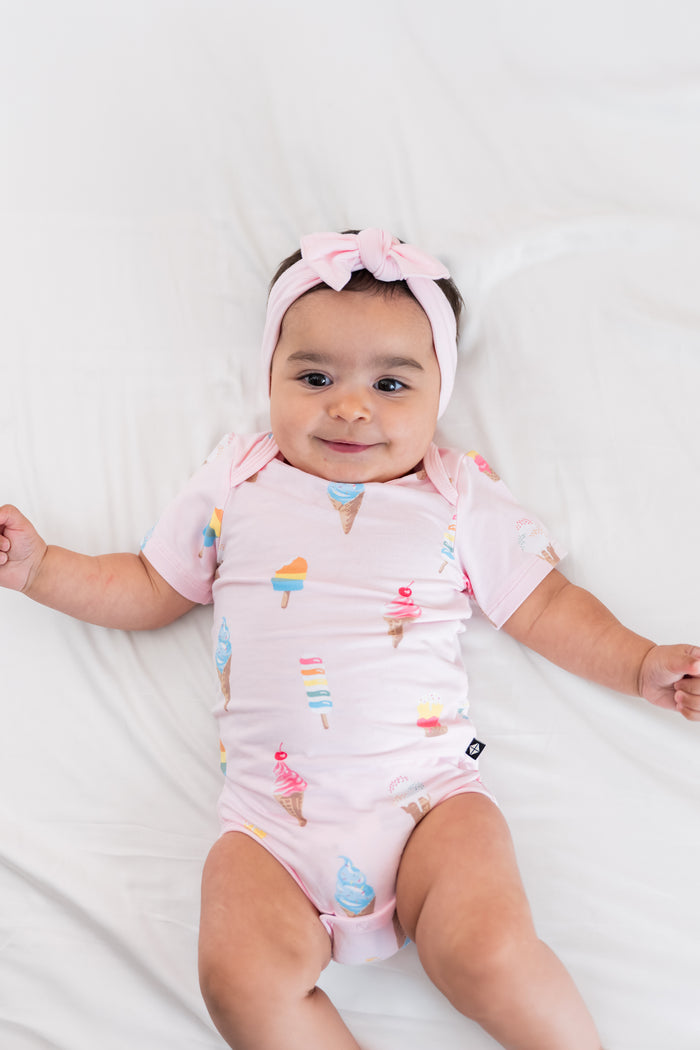 Baby wearing a Sakura Ice cream print Bodysuit with a pink bow headband on a beige background