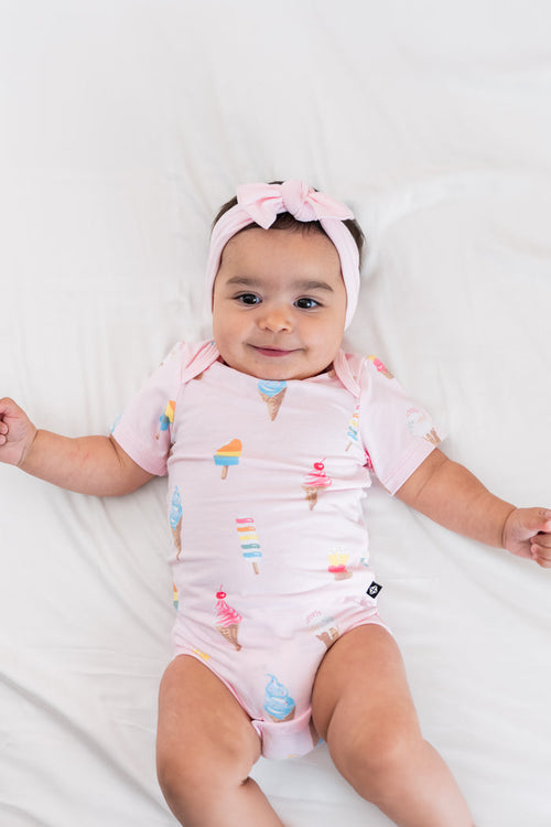 Baby wearing a Sakura Ice cream print Bodysuit with a pink bow headband on a beige background