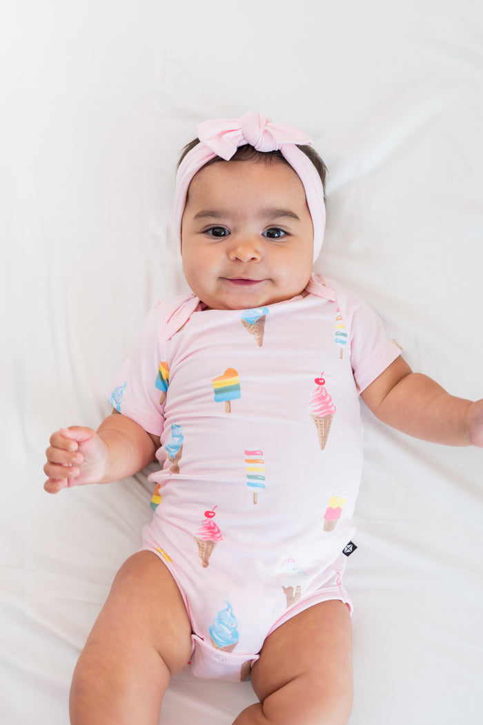 Baby smiling in a Sakura Ice cream print Bodysuit with a pink Bow headband on a beige background