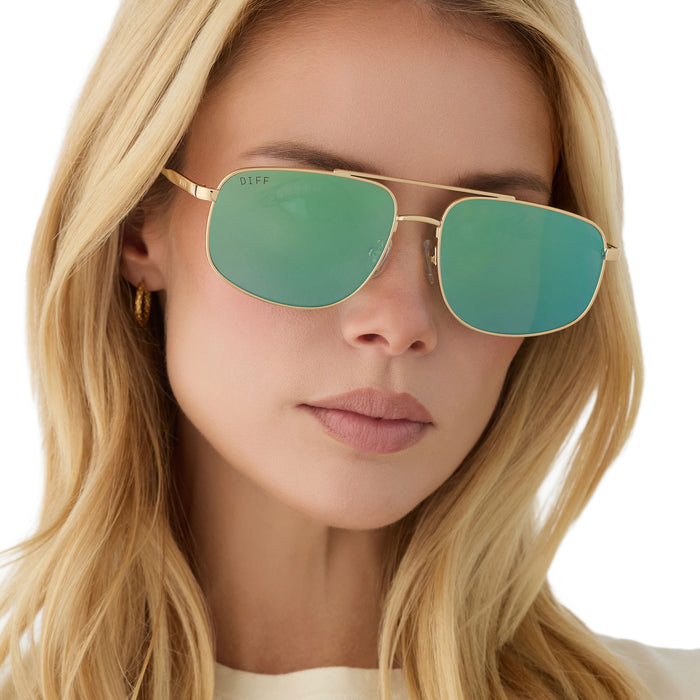 on model - blonde female wearing diff eyewear charley navigator sunglasses with a gold metal frame and dew drop blue mirrored lenses front view
