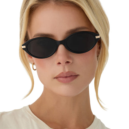 on model - blonde female wearing diff eyewear claudine oval sunglasses with a black acetate frame, gold metal temples and grey polarized lenses front view