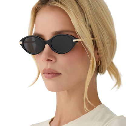 on model - blonde female wearing diff eyewear claudine oval sunglasses with a black acetate frame, gold metal temples and grey polarized lenses angled view