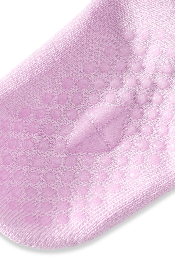 A close-up of a light pink knit sock with raised circular grip dots on the sole, shown against a plain white background.