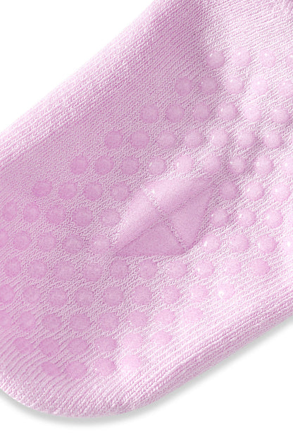 A close-up of a light pink knit sock with raised circular grip dots on the sole, shown against a plain white background.