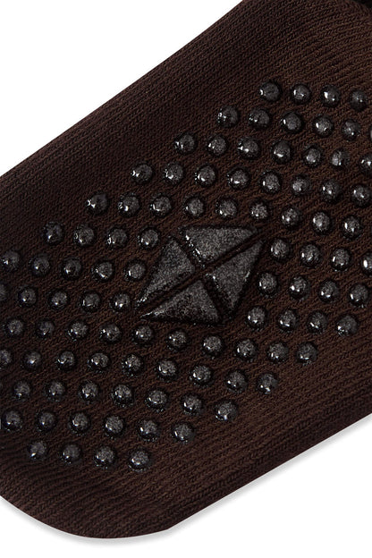 A close-up of a dark brown knit sock with black grip dots and a black triangular wedge pattern on the sole, shown against a white background.