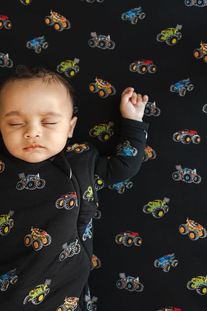 Baby wearing black Sleep Bag with Monster Truck print sleeping on a similar print crib sheet.