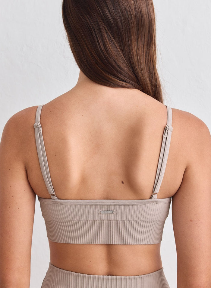 Back view of a dark clay ribbed seamless sports bra with adjustable straps and metal aim'n logo. [xs-178cm]