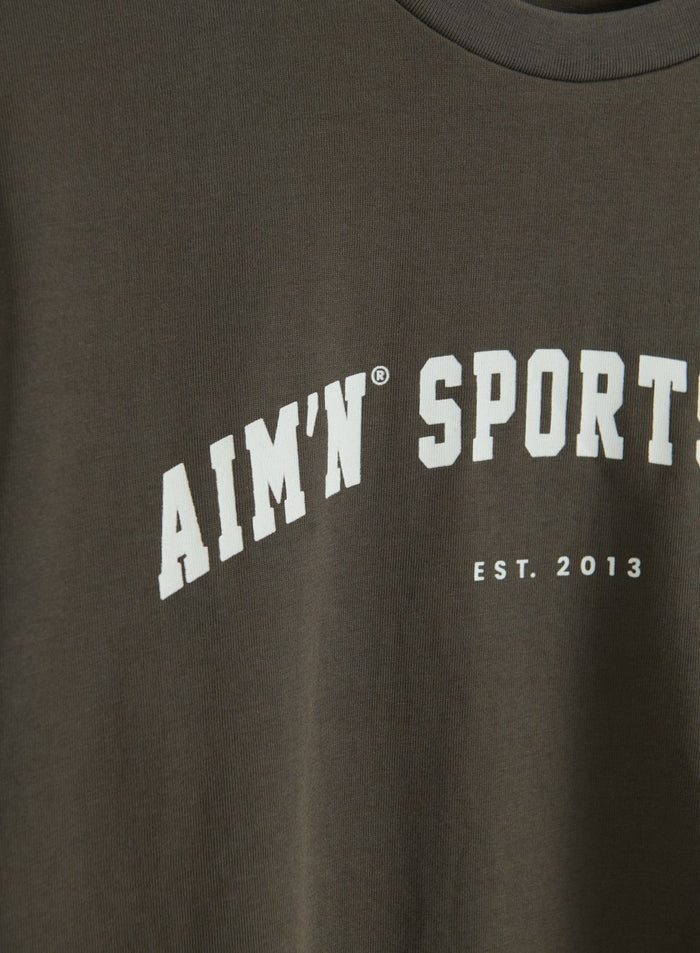 Close-up of the dark ivy Varsity Boxy T-shirt with a ribbed crew neckline and white aim'n Sport Est. 2013 graphic