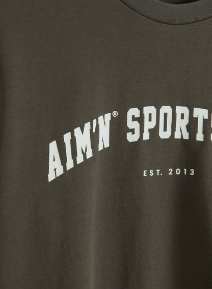 Close-up of the dark ivy Varsity Boxy T-shirt with a ribbed crew neckline and white aim'n Sport Est. 2013 graphic