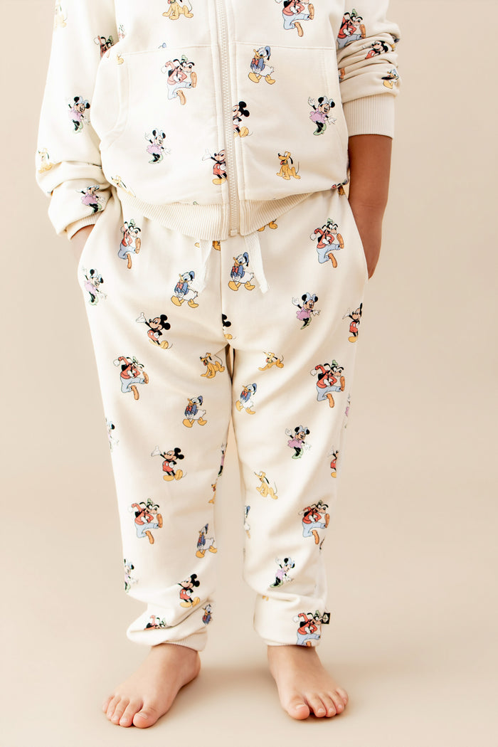 Child wearing a pair of jogger pants with a mickey and friends pattern