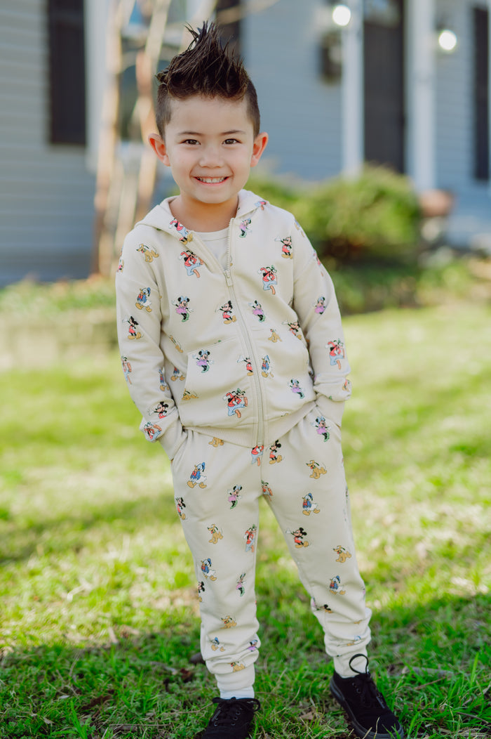 Child wearing a mickey hoodie and jogger pant standing outdoors on grass