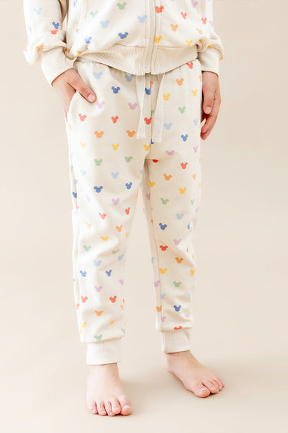 Person wearing a cream-colored jogger pant with colorful mickey patterns on a beige background