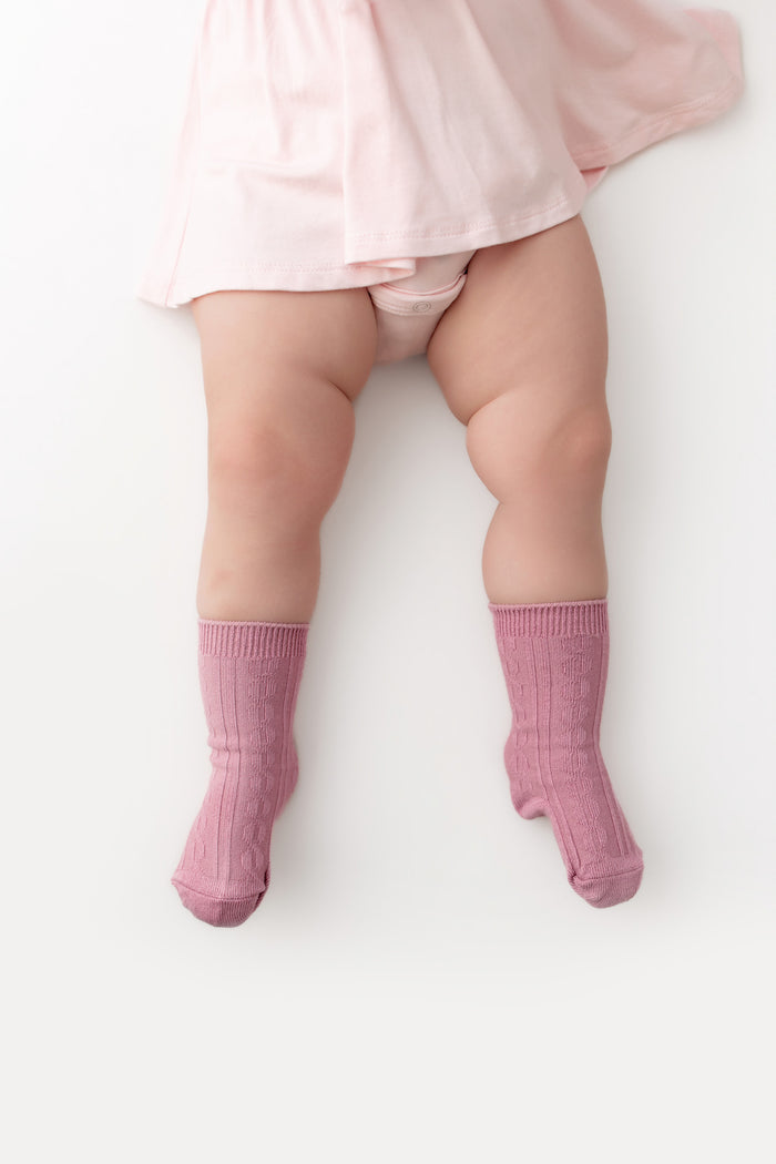 A baby's legs wearing pink ribbed crew socks and a light pink skirt, photographed from a top-down angle on a white background.
