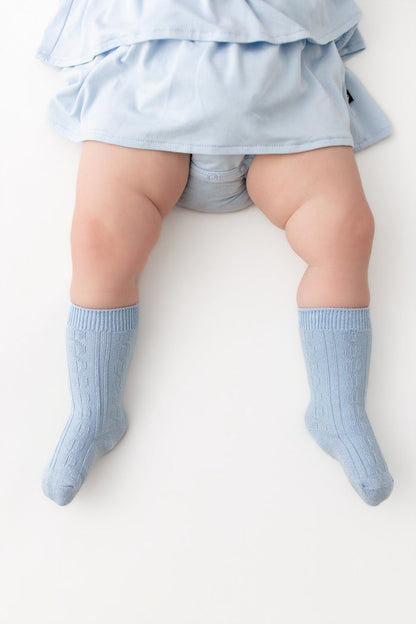 A baby's legs wearing light blue ribbed knee-high socks and a matching light blue ruffled skirt, photographed from above on a plain white background.
