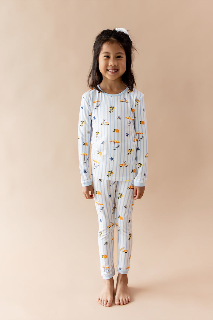 Young smiling girl standing in front of a light beige wearing the Long Sleeve Pajamas in Amalfi Coast
