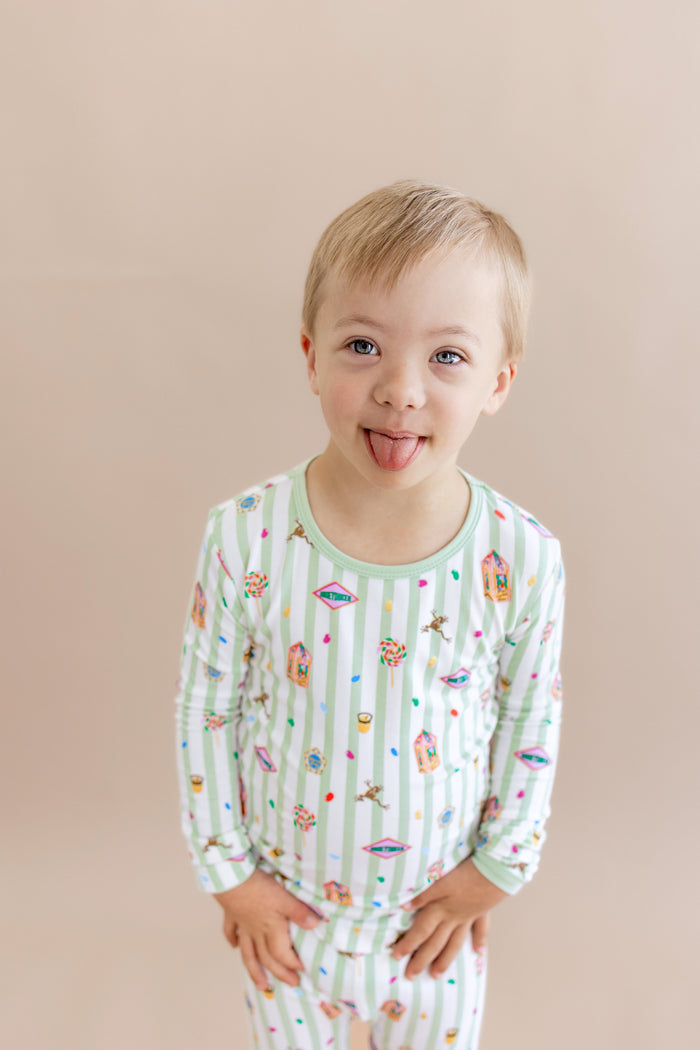 Child wearing a green and white striped long sleeve pajama set with colorful Harry Potter patterns on a beige background