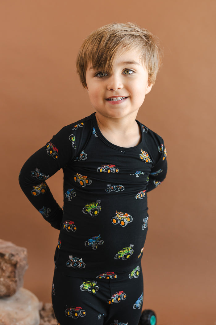 Boy smiling in black Long Sleeve Pajamas in Monster Truck print on a beige background