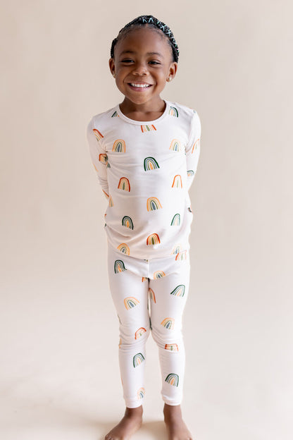 Toddler wearing Long Sleeve Pajamas in Retro Rainbow print on a beige background
