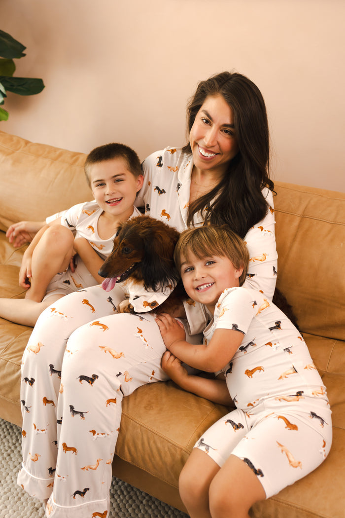 family of 3 snuggling a dog on a couch wearing matching dachshund printed pajamas