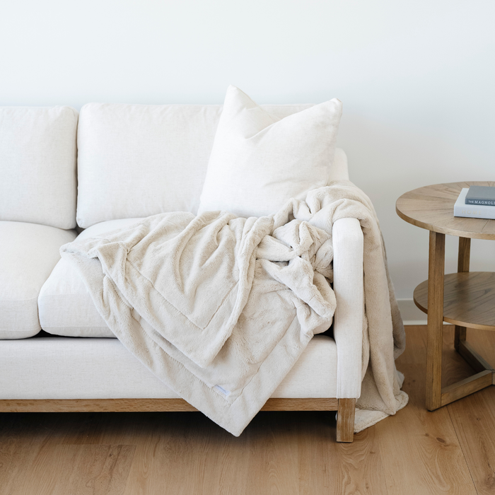 A cream blanket is draped beautifully on a couch. This lush blanket is a luxury blanket and a Saranoni blanket. Enjoy this extra large blanket as a home decor staple, as a comfort gift, or for relaxation. Embrace luxury that lasts with this soft blanket.